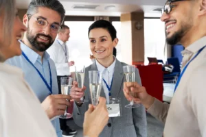 Grupa elegancko ubranych osób na spotkaniu biznesowym, wznosząca toast kieliszkami szampana. W tle nowoczesne wnętrze z jasnym oświetleniem, sprzyjające networkingowi.